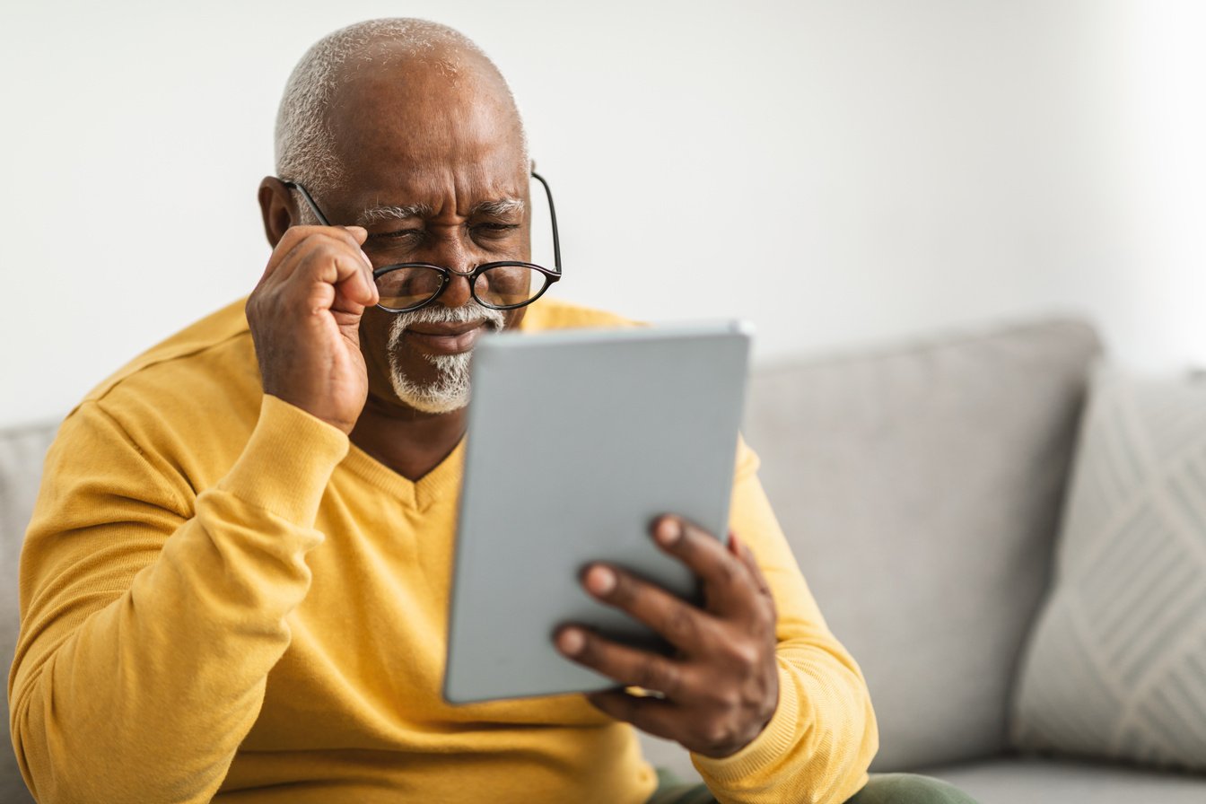 Senior Man with Poor Eyesight Using Tablet Squinting Eyes Indoor